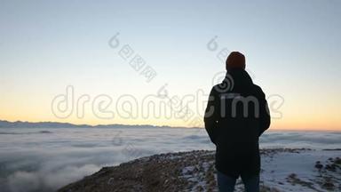 从后面看。 一个孤独的人站在高高的山上，看着夕阳和夕阳的地平线